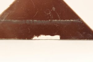 Brown ceramic triangle tile with a shiny surface, showing visible wear, scratches, and a chipped edge.