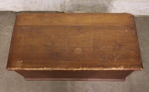 Top view of a dark wood tone cedar chest with visible wear, including scuffs and a damaged lid edge.