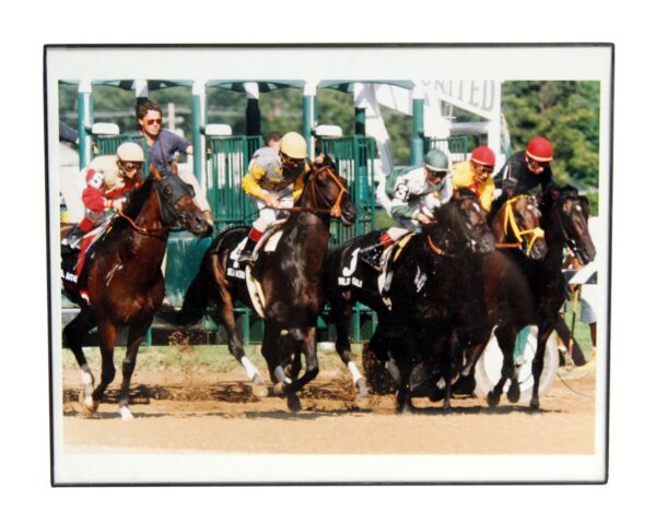 Vintage framed horse racing photo in a black plastic frame, showing jockeys on horses at the start of a race.