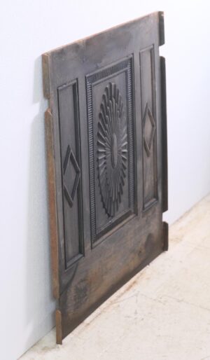 Antique Federal black cast iron fireplace fire back shown at an angle, with a central sunburst relief and side diamond panels, plus a visible crack in the lower section.