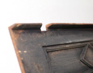 Close-up of an antique Federal cast iron fireplace fire back with a black finish, showing the upper edge and carved detail.