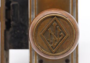 Close-up of a bronze entry door knob with a raised LN emblem in a diamond motif and visible age wear.