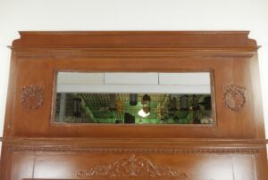 Antique Victorian dark wood mantel with an overmantel mirror and ornate carved detailing, shown in a front view with visible minor surface chips and predrilled holes.