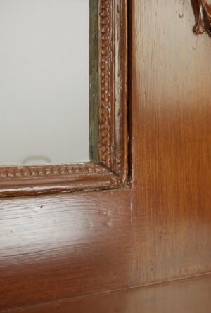 Close-up of an antique Victorian wooden mantel mirror frame in a dark wood tone, showing ornate carved detailing and minor surface wear.