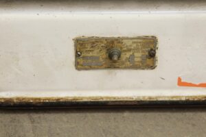 Close-up of a white enamel metal scale with a worn identification plate and adjustment knob.