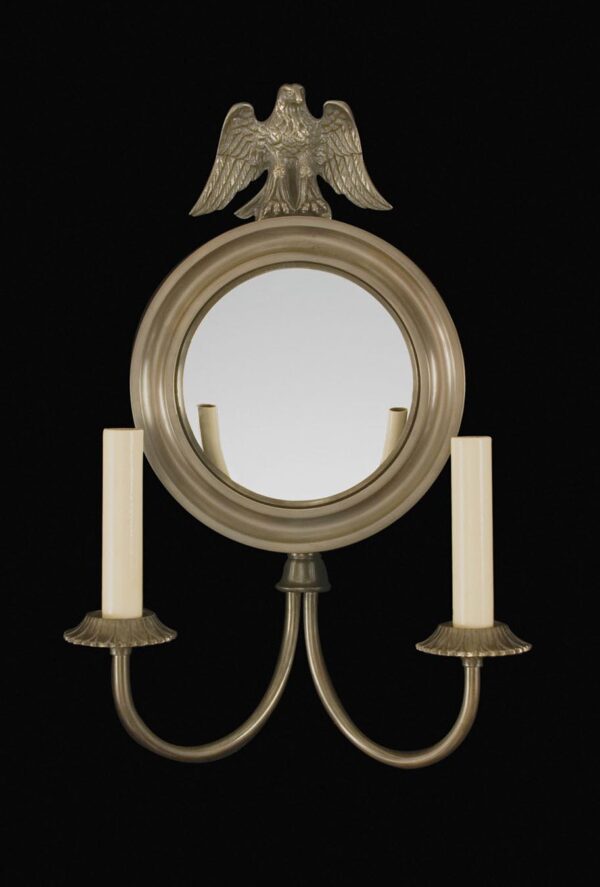 Colonial wall sconce with a round mirrored back plate, decorative eagle crest, and two candle-style arms in oil rubbed bronze finish.