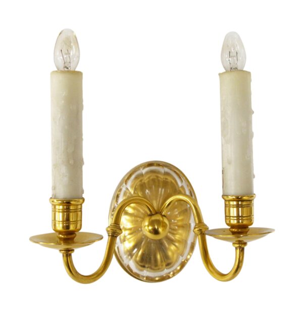Georgian-style two-arm wall sconce with a polished brass frame, clear cut crystal oval backplate, and two candle-style lights.