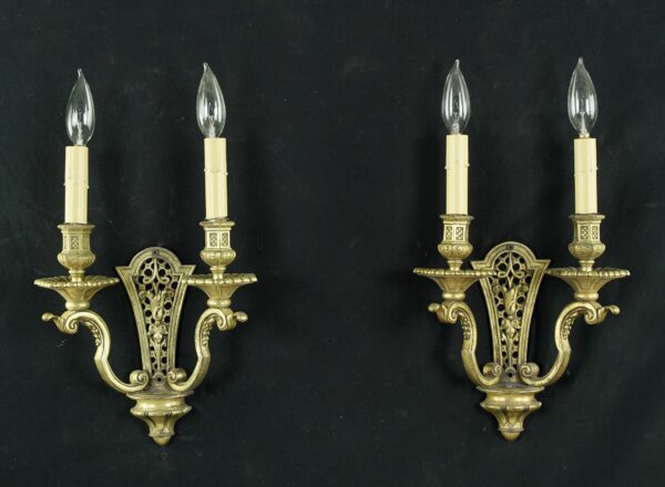 Pair of antique French brass wall sconces with two arms each, shown as a matching pair with tulip-shaped candle holders, lattice details, and clear candle-style bulbs.