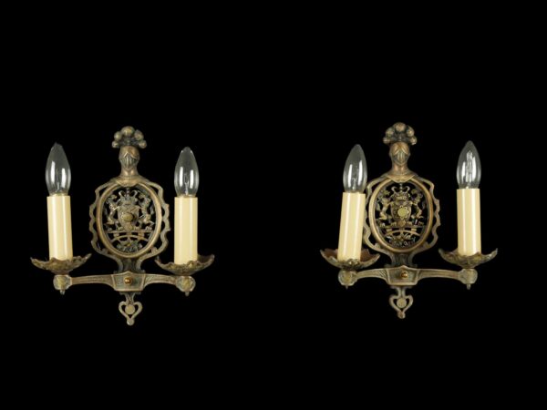 Pair of bronze two-arm wall sconces with knight head and coat of arms motifs, each shown with two candle-style bulbs.