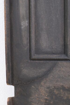 Close-up of an antique Federal cast iron fireplace fire back with a black finish, showing a recessed panel and a visible crack near the lower edge.