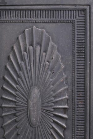 Close-up of a Federal cast iron fireplace fireback with a fan motif and one visible crack on the right side.