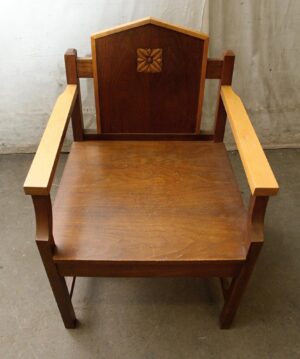 Mission style wood chair with dark and light wood tones, a square carved floral motif on the backrest, and straight arms shown from the front.