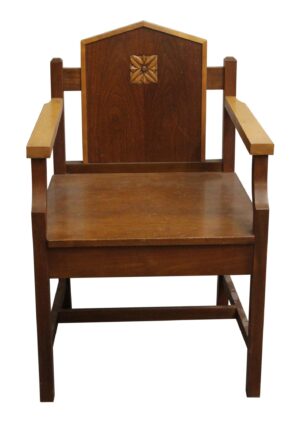 Mission-style wood chair with dark and light wood tones, a carved floral motif on the backrest, straight arms, and a simple slatted frame.