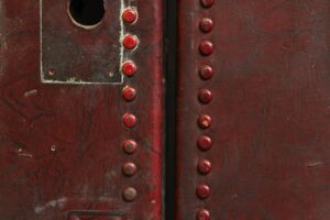 Close-up of a red leather studded door with a rectangular inset and a circular opening near the top left.