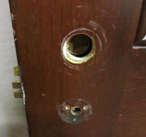 Close-up of a dark wood tone door showing a circular hardware cutout and lower lock holes, with minor wear visible on the surface.