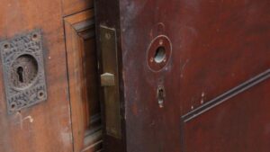 Close-up of a six-panel door with antique-style hardware and a visible mortise lock opening, shown in a dark wood tone.