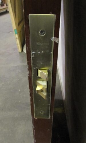 Close-up of a dark wood tone door edge showing a brass latch plate and strike hardware.