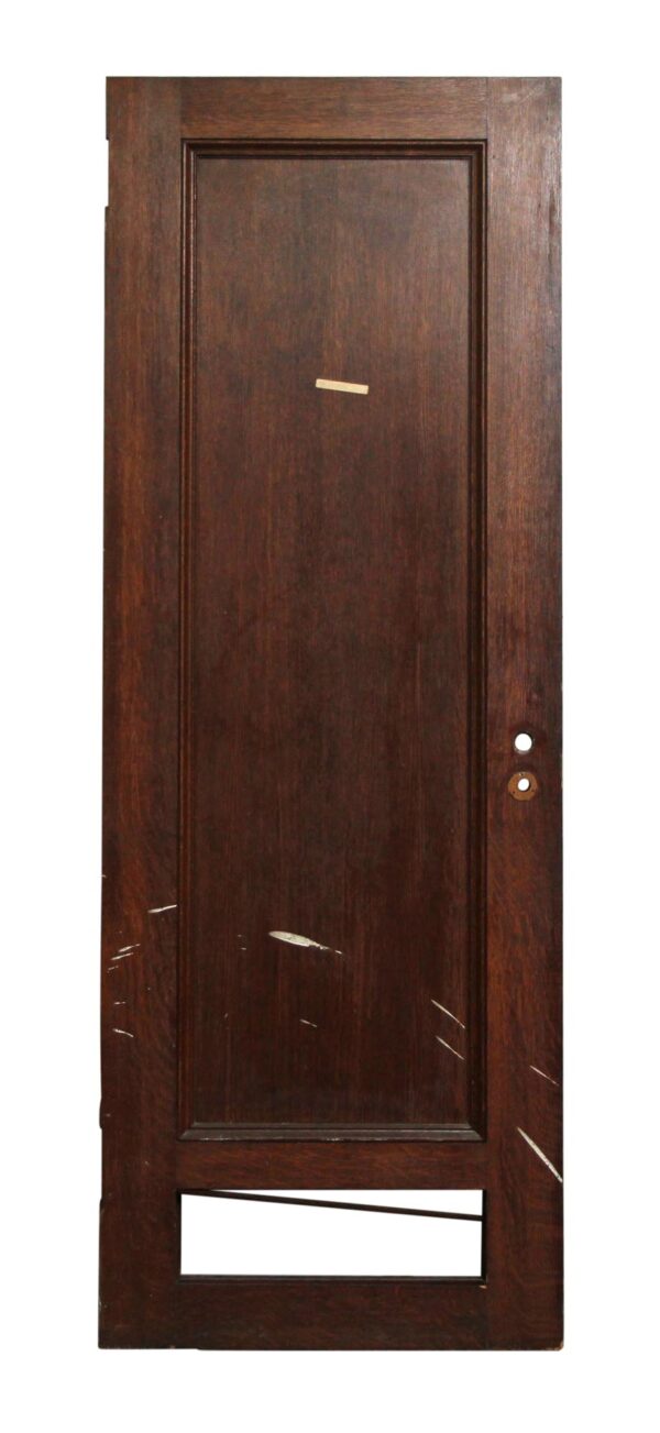 Single-panel wood door in a dark wood tone with a bottom cutout and visible hardware holes on the right side.
