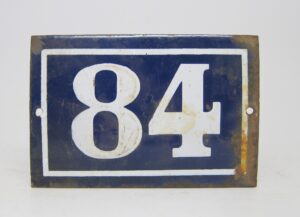Blue and white enamel number 84 sign with a rectangular shape, white border, and visible wear and rust.