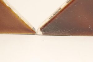 Close-up of two brown ceramic triangle tiles with a shiny surface, showing chipped edges and visible wear where they meet at the center.