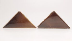Two brown shiny ceramic triangle tiles with visible surface wear and small chips, shown side by side.