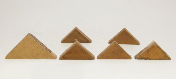Six tan ceramic triangular tiles in varying sizes, arranged with visible age-related chips and surface wear.