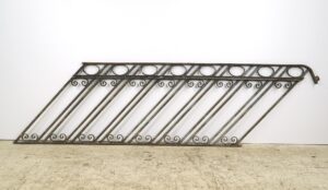 Reclaimed cast iron staircase railing with diagonal bars, scroll details, and a weathered gray and black rusted finish.