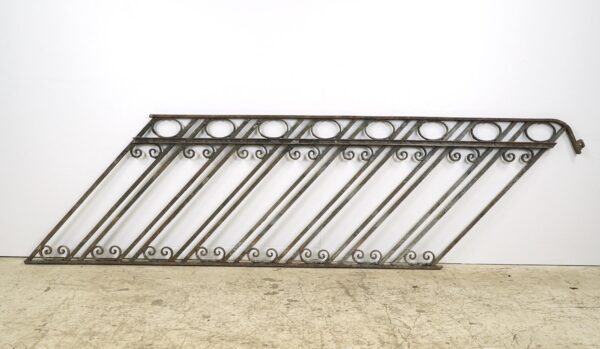 Reclaimed cast iron staircase railing with diagonal bars, scroll details, and a weathered gray and black rusted finish.