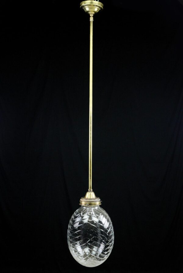 Pendant light with a long brass pole and a clear egg-shaped etched crystal globe.