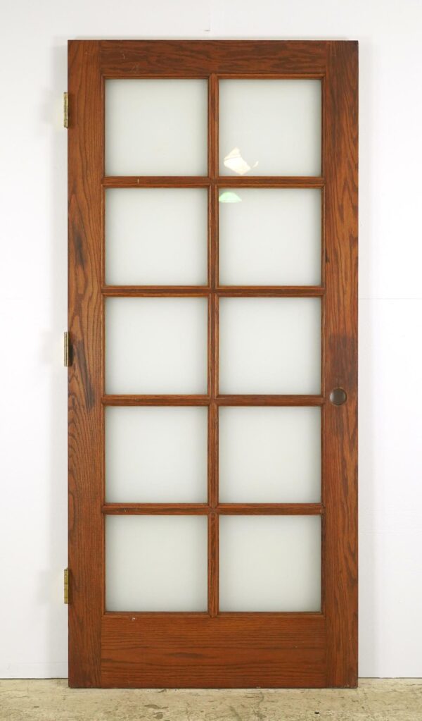Vintage oak French door with ten frosted glass panes and brass hinges.