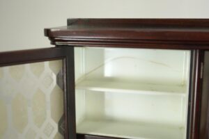 Close-up of the mahogany cabinet showing the white milk glass shelving and part of an embossed glass door beneath the mirrored top.