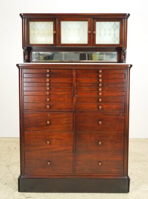 1920s mahogany dental cabinet with 22 drawers, embossed glass doors, a milk glass top, and a mirrored backsplash.