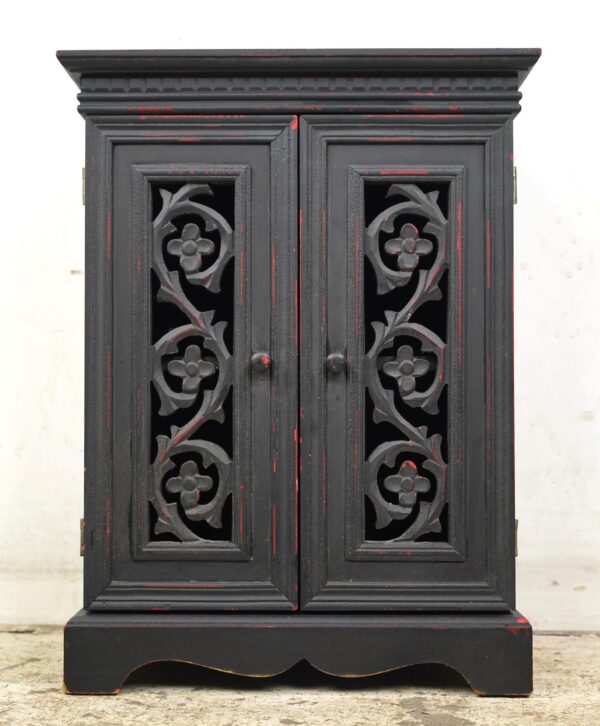 Front view of a small black wood storage cabinet with two carved doors, red distressed highlights, and a decorative base.