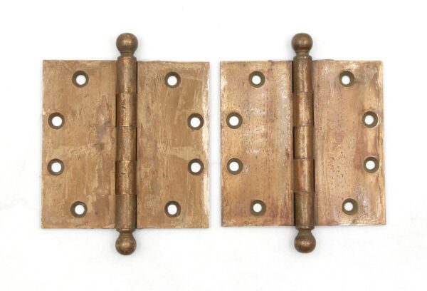 Pair of brass butt door hinges shown side by side, each with ball tips, five knuckles, and multiple mounting holes, with visible surface wear and an antique finish.