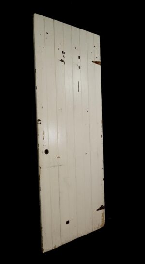 Antique white wood passage door with four vertical boards and visible paint wear, shown at an angle.