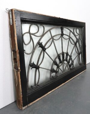 Antique fanlight transom window with a black frame, radiating metal bars, raised floral intersections, and mounting hardware on the side.