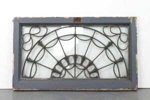 Antique fanlight transom window with a semi-circular leaded design, painted gray on one side, showing mounting hardware and a visible crack in the glass.