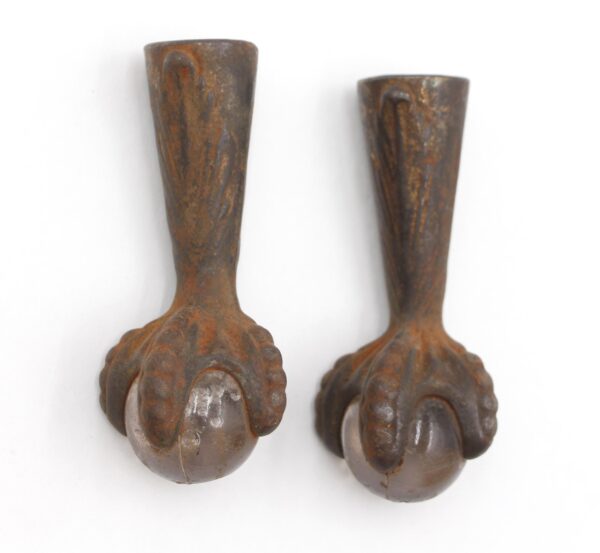 Pair of antique cast iron furniture feet with black claw details gripping clear glass balls, shown as a pair.