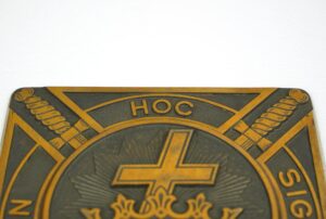 Close-up of a brass plaque with an antique brass and black finish, showing the top section of a Masonic Knights Templar design with crossed swords and the text HOC.