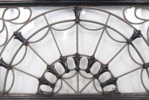 Fanlight transom window with a semi-circular leaded design, raised floral details, and a visible crack in the glass.