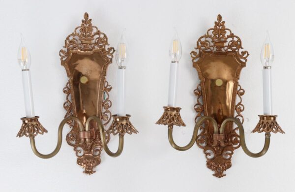 Pair of bronze two-arm wall sconces with ornate scrollwork back plates and candle-style bulbs.