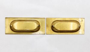 Pair of polished brass sash lifts shown side by side, each with an oval recessed handle and rectangular backplate.