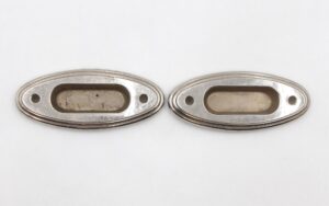 Pair of oval recessed window sash lifts shown side by side, with nickeled brass finish and two screw holes each.