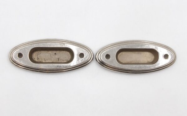 Pair of oval recessed window sash lifts shown side by side, with nickeled brass finish and two screw holes each.