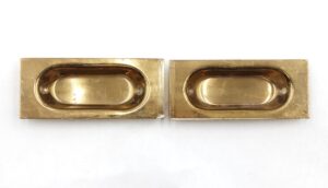 Pair of polished brass sash lifts shown side by side, each with an oval recessed pull and mounting holes on a rectangular backplate.