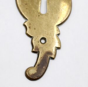 Close-up of a French-style brass door back plate with a double keyhole and visible surface wear.