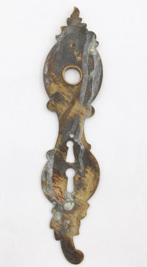 Vintage brass door back plate with an ornate French-style shape, double keyhole cutouts, and visible surface wear from prior use.