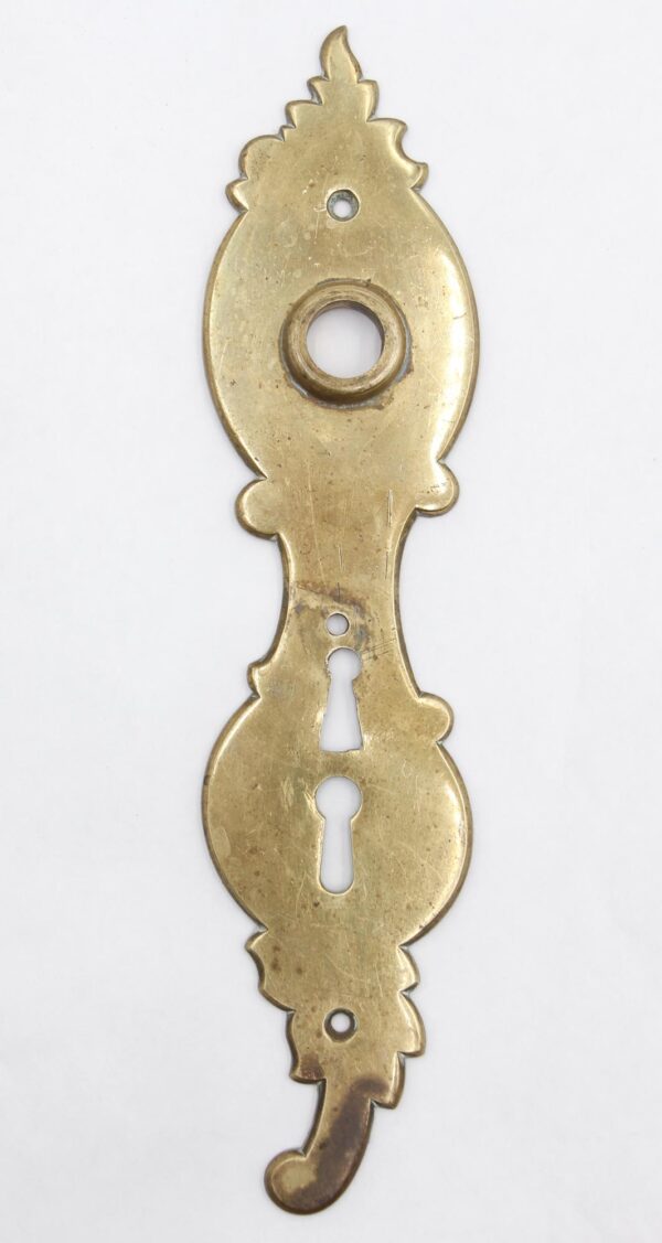 French-style brass door back plate with a polished finish, a double keyhole, and a decorative elongated shape with visible mounting holes.