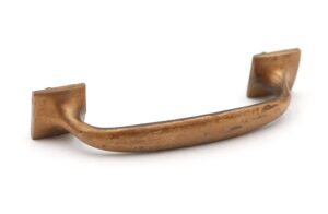 Antique brass bridge drawer pull with a curved handle and square mounting ends, shown at an angle to reveal the worn patina and used condition.