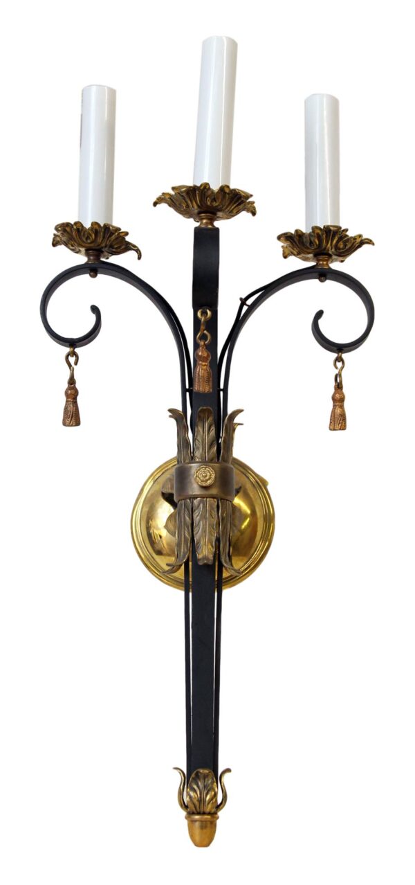 French-style three-arm wall sconce with black cast iron scrollwork, polished brass accents, and three candle-shaped bulb holders.